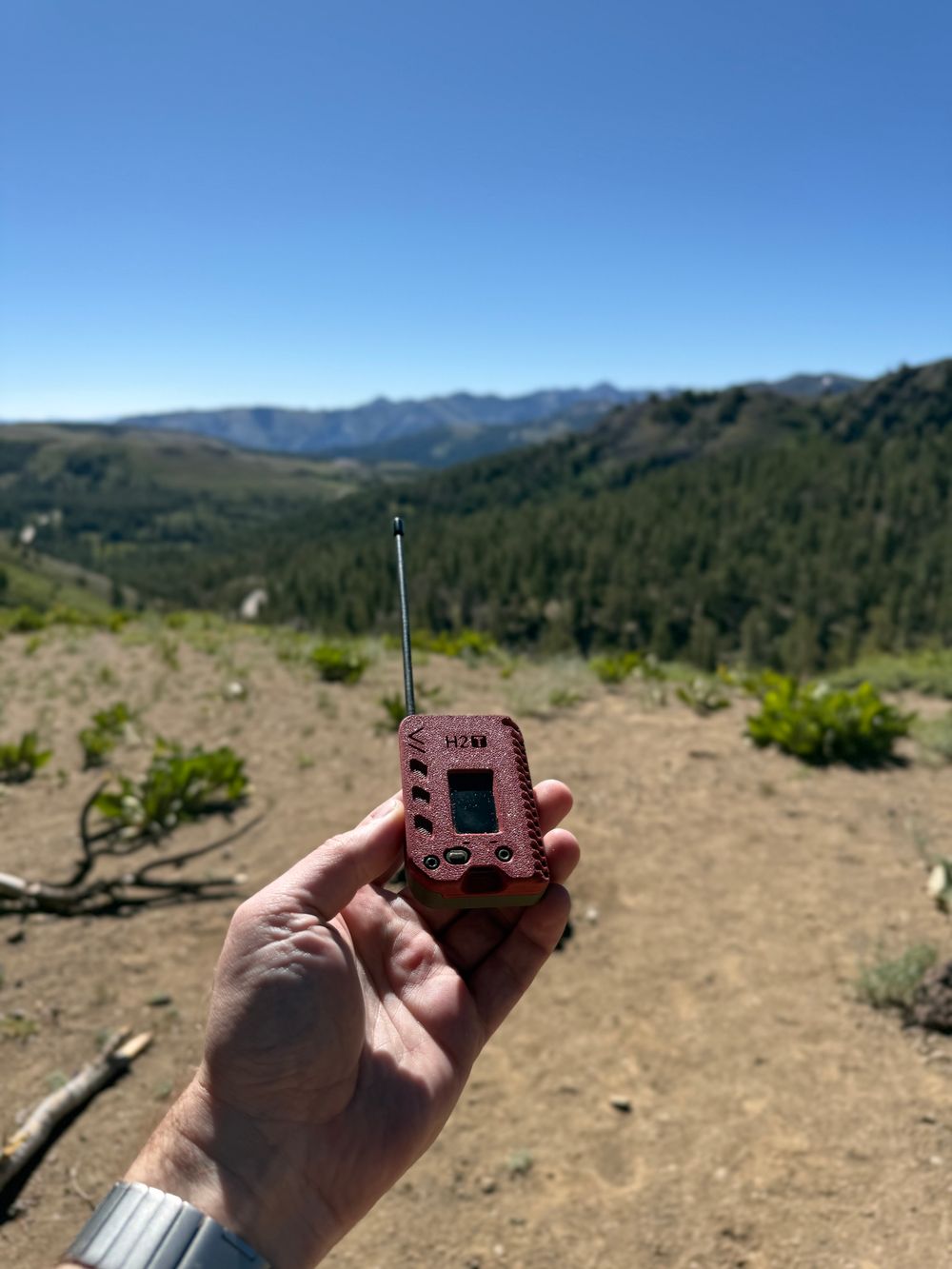 A hand holding a Meshtastic radio on top of a mountain pass