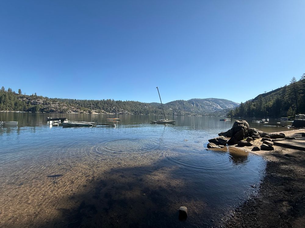 A lake with clear water and blue skies and mountains surrounding it